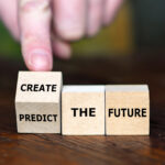 Hand positioning wooden blocks spelling 'CREATE THE FUTURE' on wooden surface.