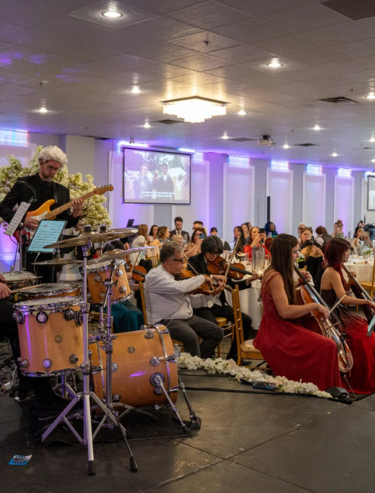 Live band performing with guitar, drums, and violins at a Heritage Banquet Hall celebration with purple accent lighting